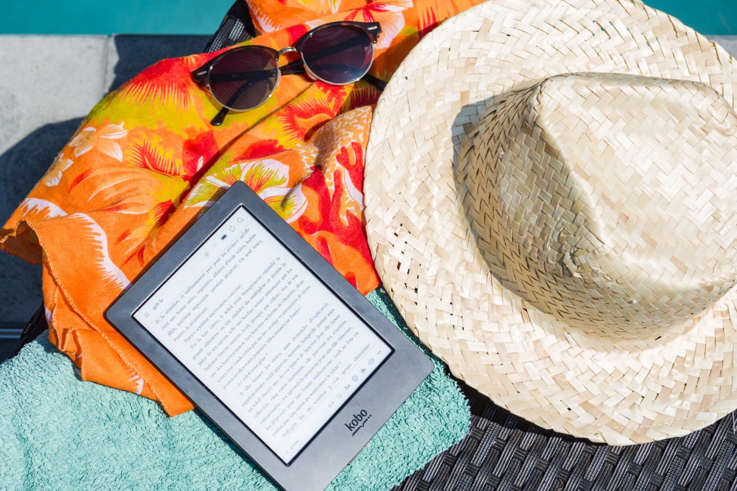 A teacher's kindle and hat in summer by a pool